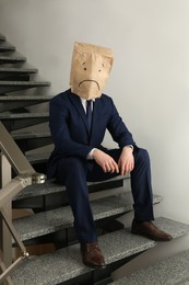 Photo of Man wearing paper bag with drawn sad face indoors