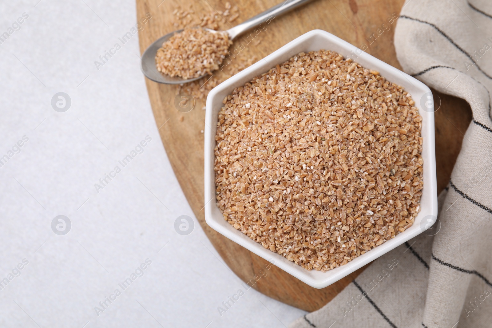 Photo of Dry wheat groats in bowl and spoon on light table, top view. Space for text