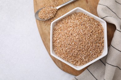 Photo of Dry wheat groats in bowl and spoon on light table, top view. Space for text