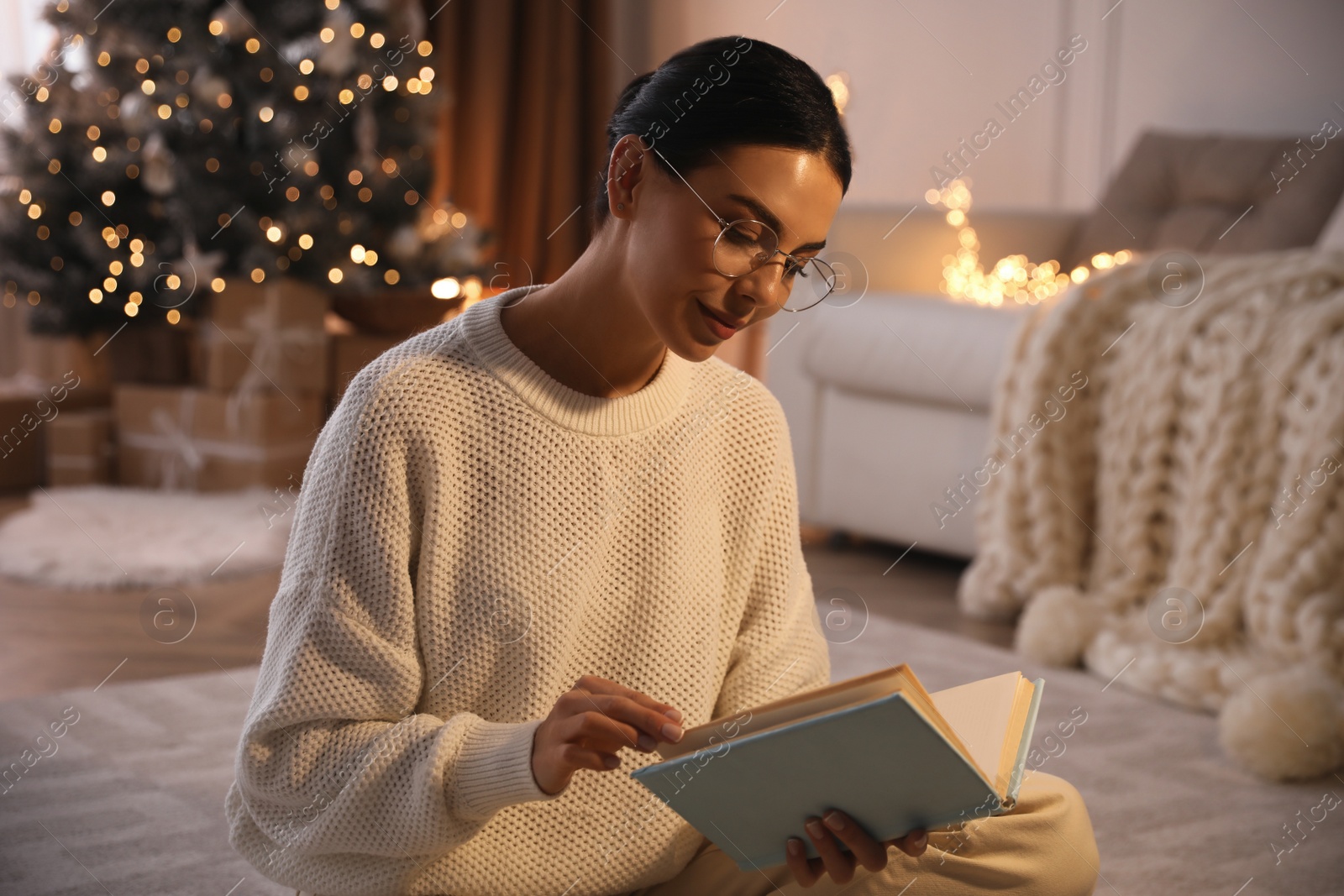 Photo of Young woman reading book at home. Christmas celebration