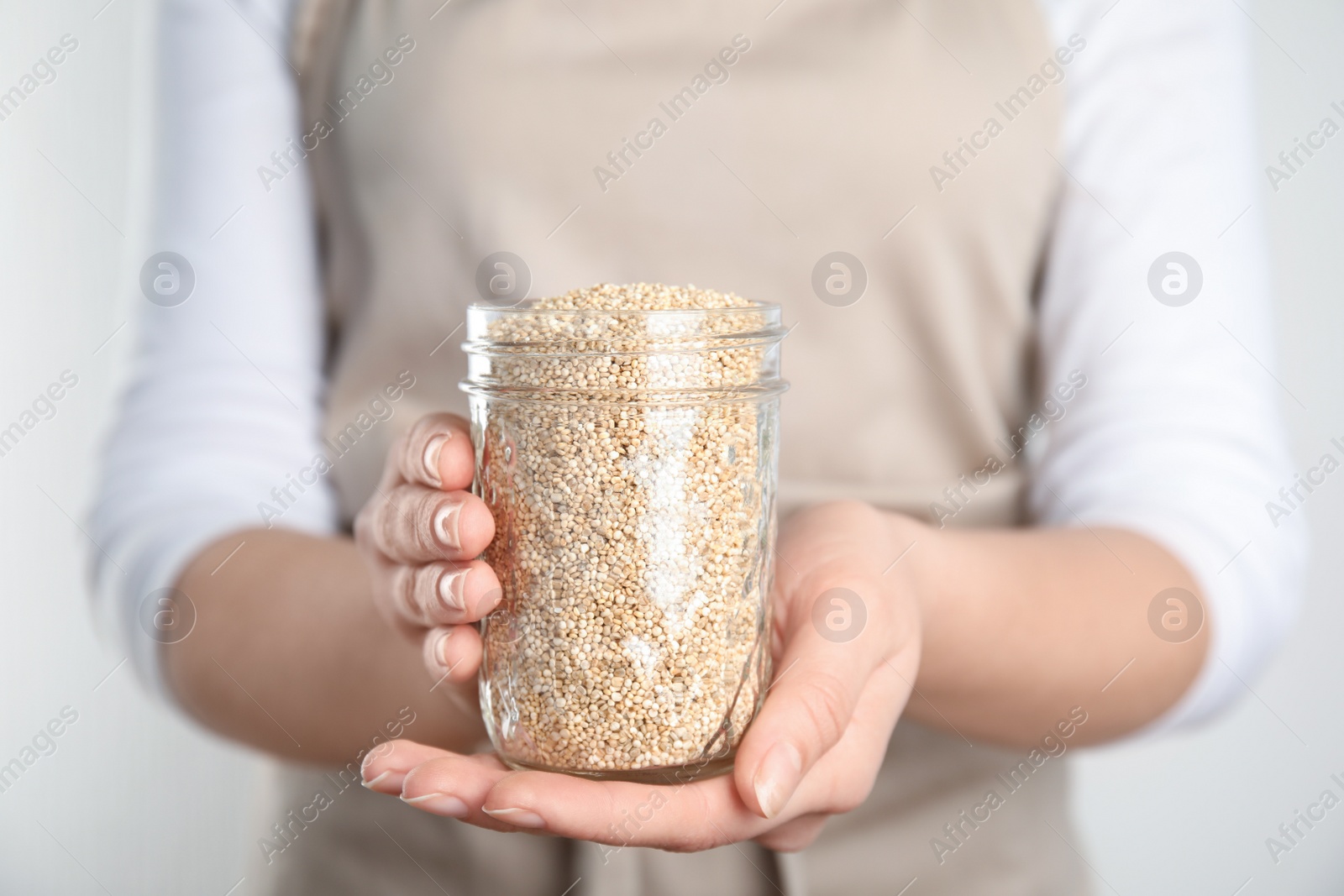Photo of Woman holding jar with white quinoa on light background, closeup