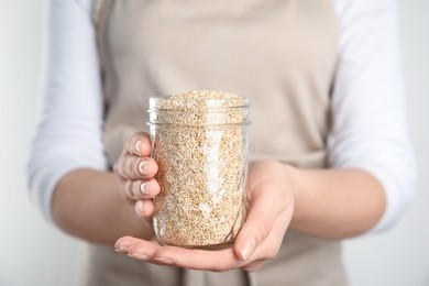 Woman holding jar with white quinoa on light background, closeup