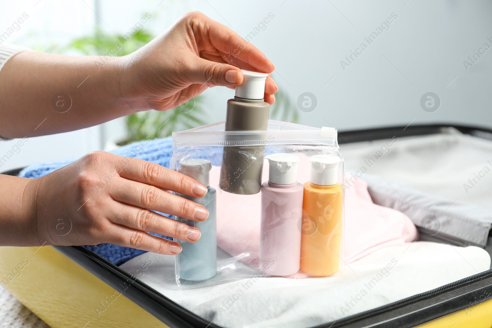 Photo of Woman with plastic bag of cosmetic travel kit packing suitcase, closeup