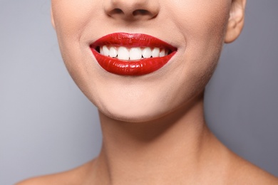 Photo of Beautiful young woman with red glossy lips on gray background, closeup