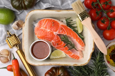 Fresh fish, lime, rosemary and marinade in baking dish surrounded by products on light table, flat lay