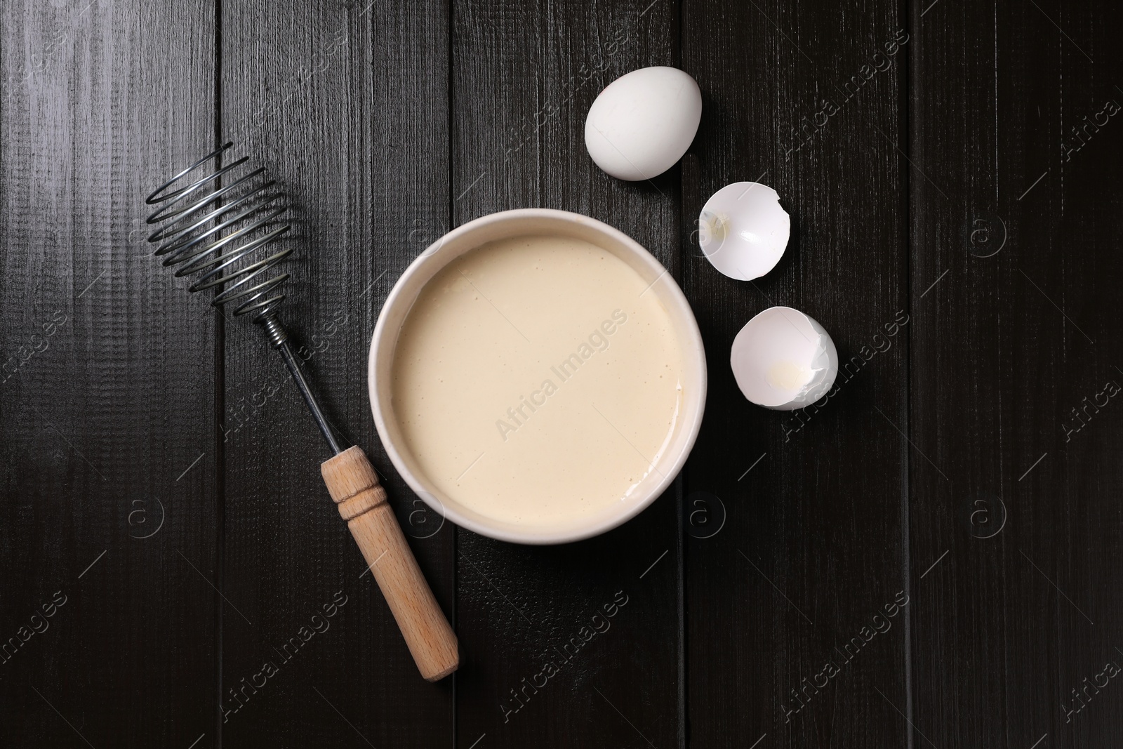 Photo of Metal whisk, dough in bowl, egg and shell on wooden table, flat lay