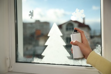 Woman using snow spray for decorating window at home, closeup