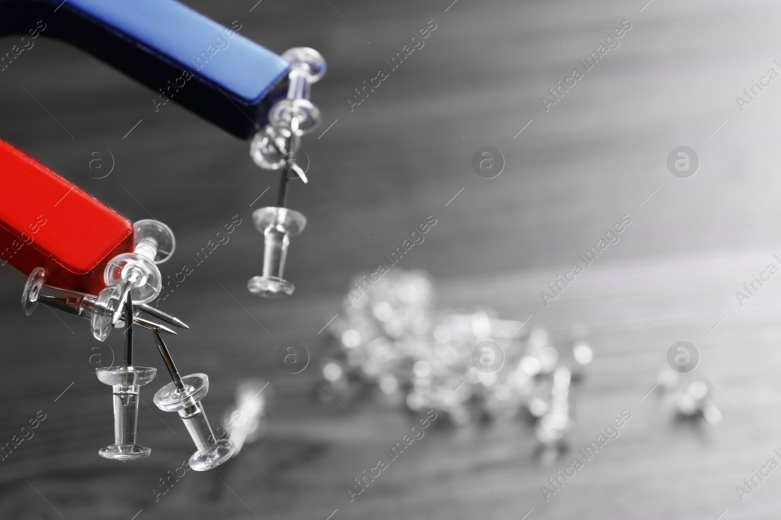 Photo of Magnet attracting drawing pins on dark grey wooden background, closeup. Space for text