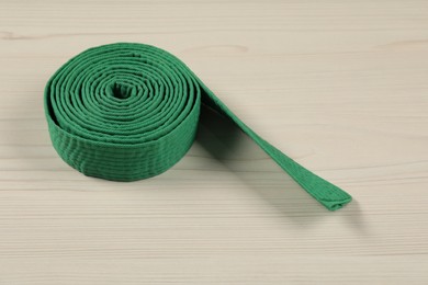 Photo of Green karate belt on wooden background. Martial arts uniform