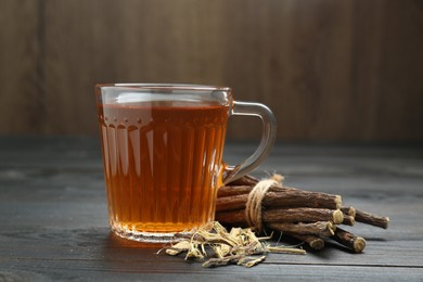 Photo of Aromatic licorice tea in cup and dried sticks of licorice root on black wooden table