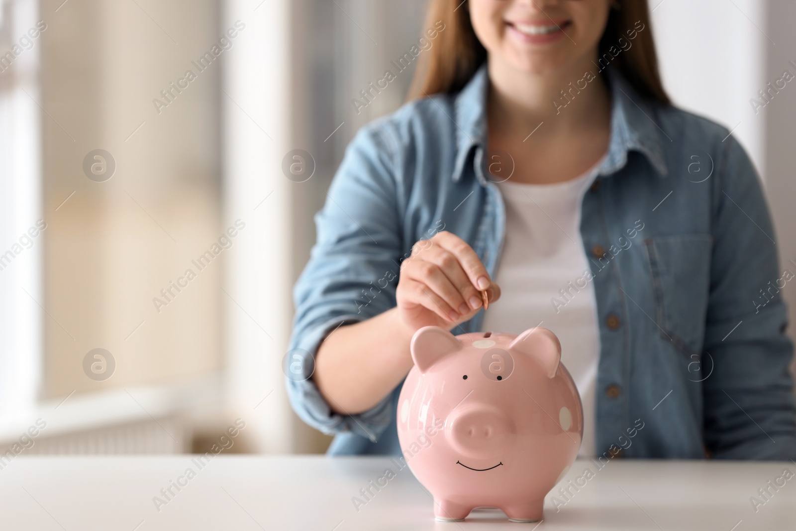 Photo of Woman putting coin into piggy bank at table indoors, closeup. Space for text