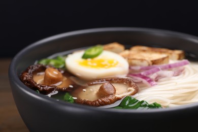 Delicious vegetarian ramen in bowl on table against black background, closeup