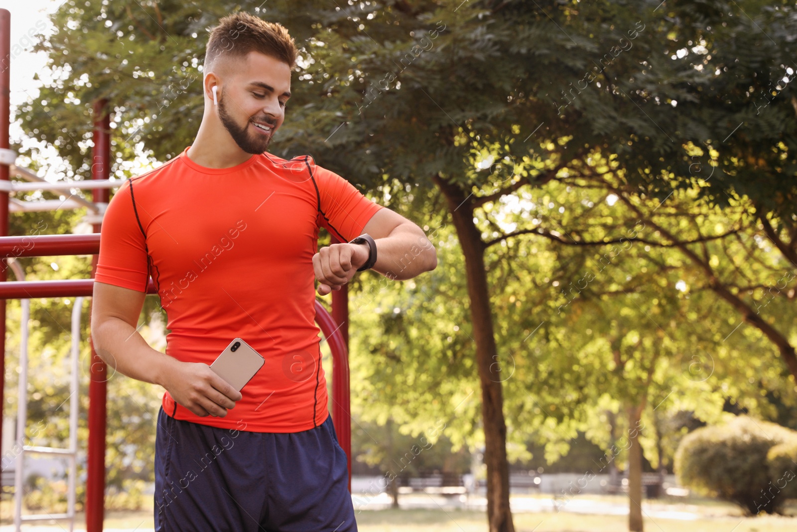 Photo of Young man with wireless headphones and mobile device listening to music on sports ground. Space for text