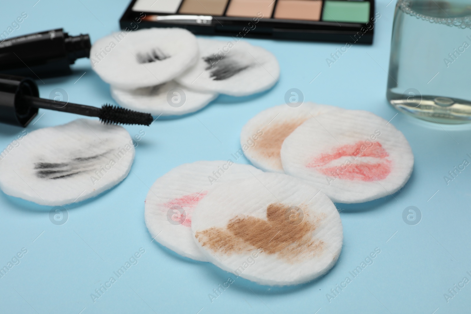 Photo of Dirty cotton pads after removing makeup and different cosmetic products on light blue background, closeup