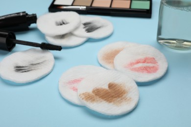 Dirty cotton pads after removing makeup and different cosmetic products on light blue background, closeup