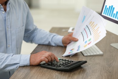 Professional accountant using calculator at wooden desk, closeup