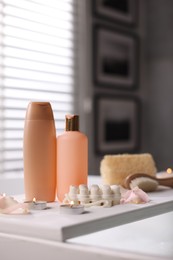 Wooden tray with toiletries and flower petals on bathtub in bathroom