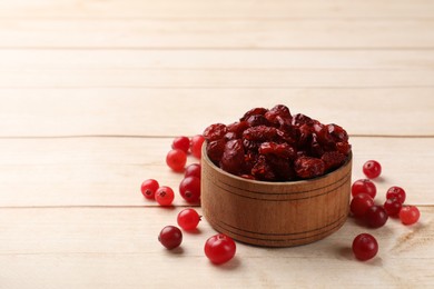 Photo of Dried cranberries in bowl and fresh berries on wooden table, space for text