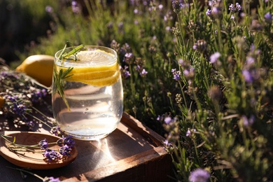 Photo of Glass of fresh lemonade on wooden tray in lavender field. Space for text