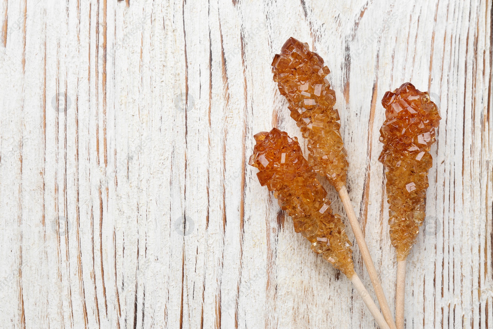 Photo of Sticks with sugar crystals on white wooden table, flat lay and space for text. Tasty rock candies