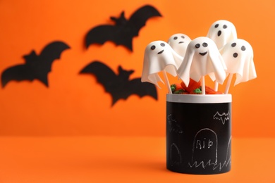 Photo of Delicious ghost shaped cake pops on orange background, space for text. Halloween celebration