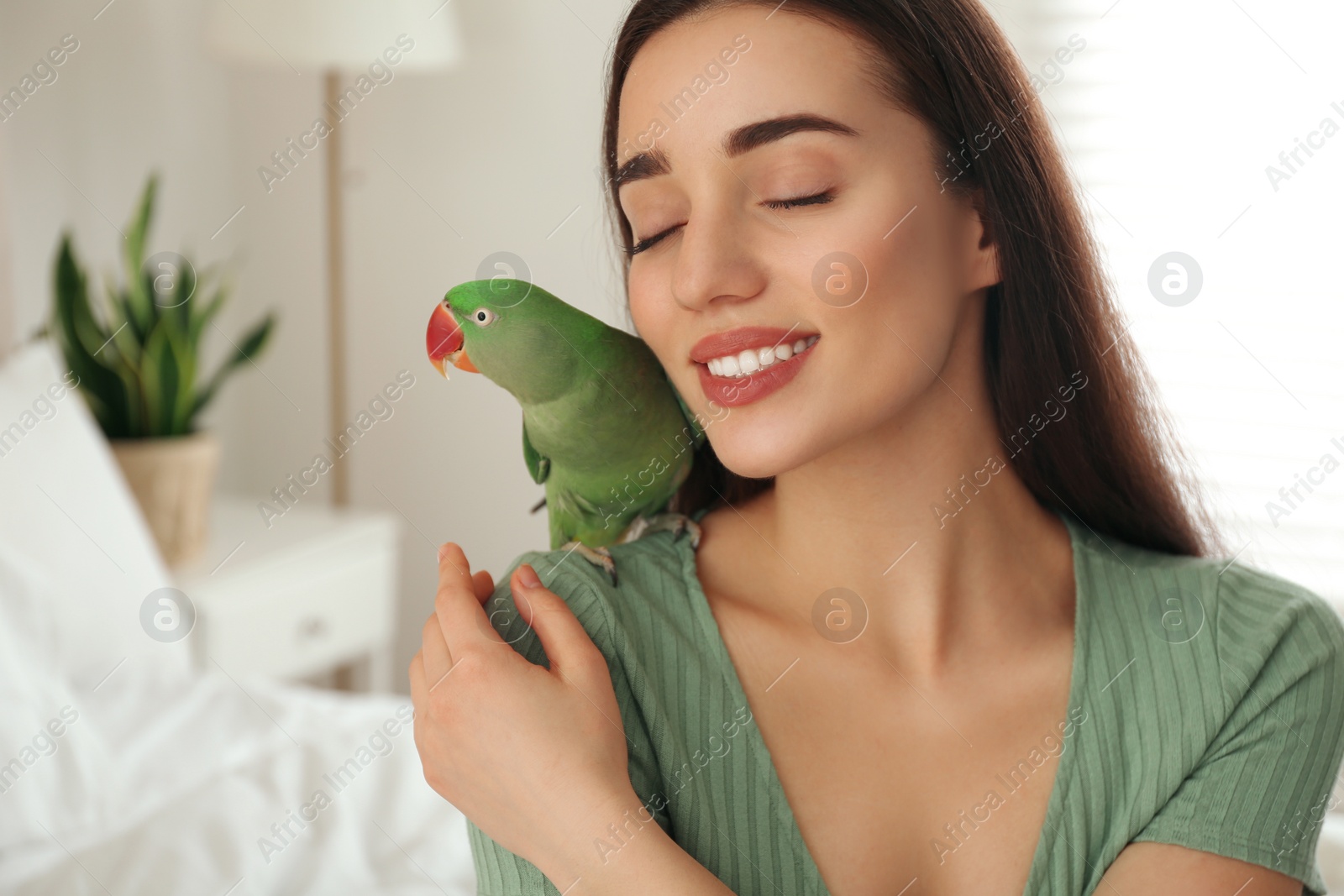 Photo of Young woman with Alexandrine parakeet indoors. Cute pet