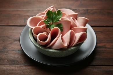 Photo of Slices of delicious boiled sausage with parsley on wooden table, closeup