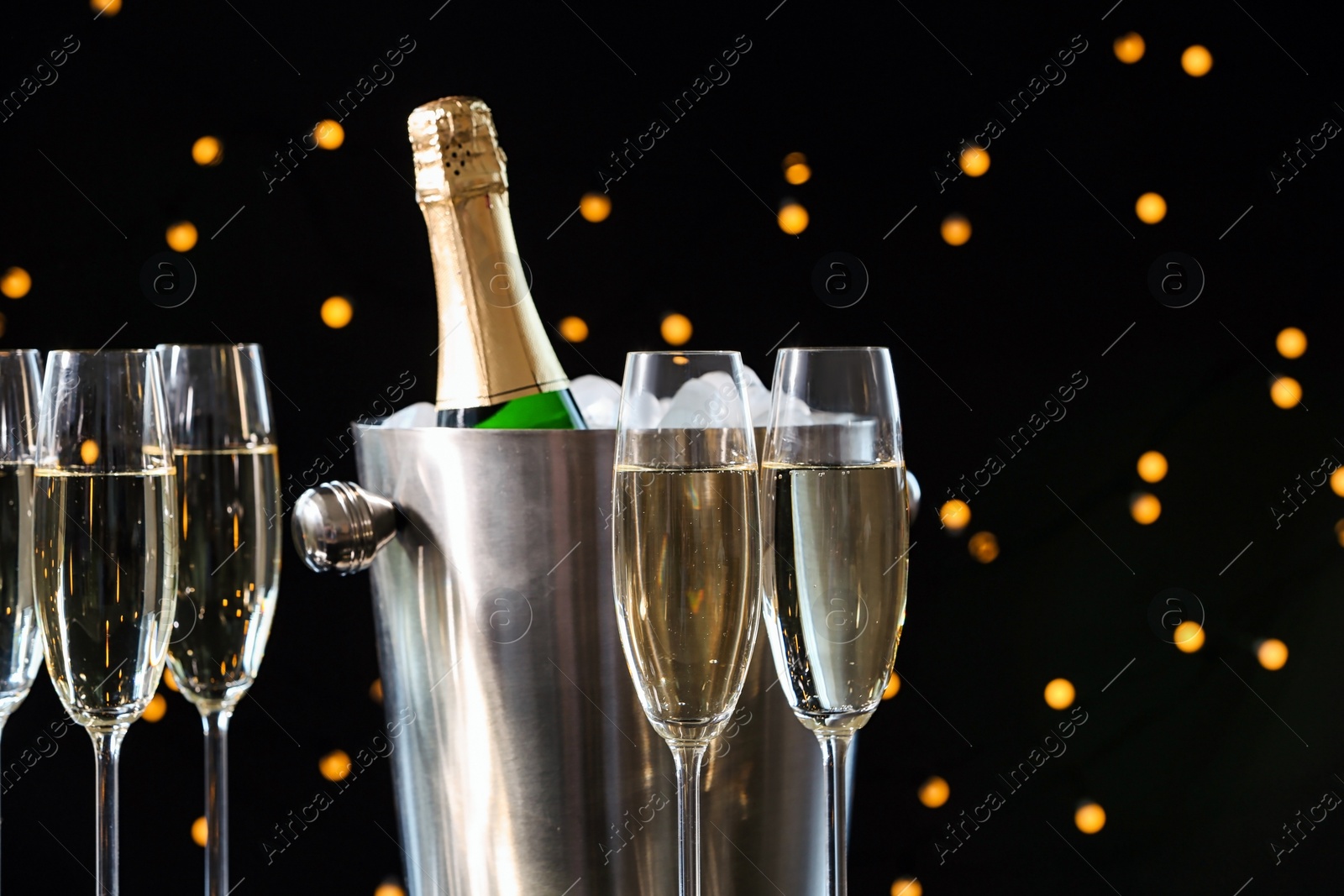 Photo of Glasses with champagne and bottle in bucket against blurred lights