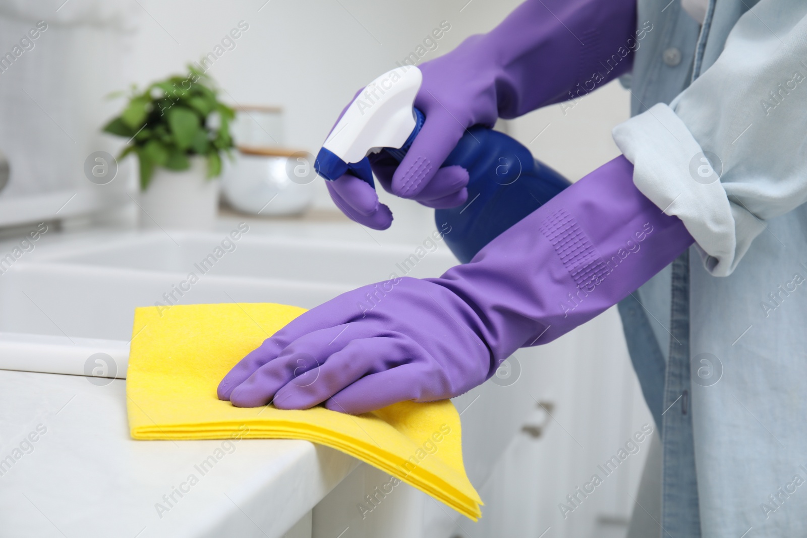 Photo of Woman cleaning white countertop with rag and detergent indoors, closeup