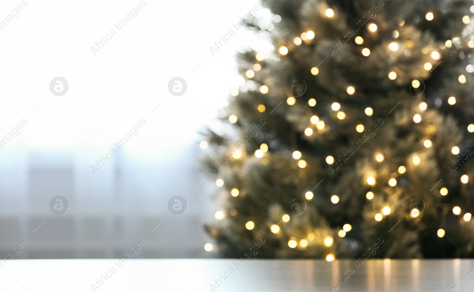 Photo of Blurred view of beautiful Christmas tree with yellow lights near window indoors, focus on table. Space for text