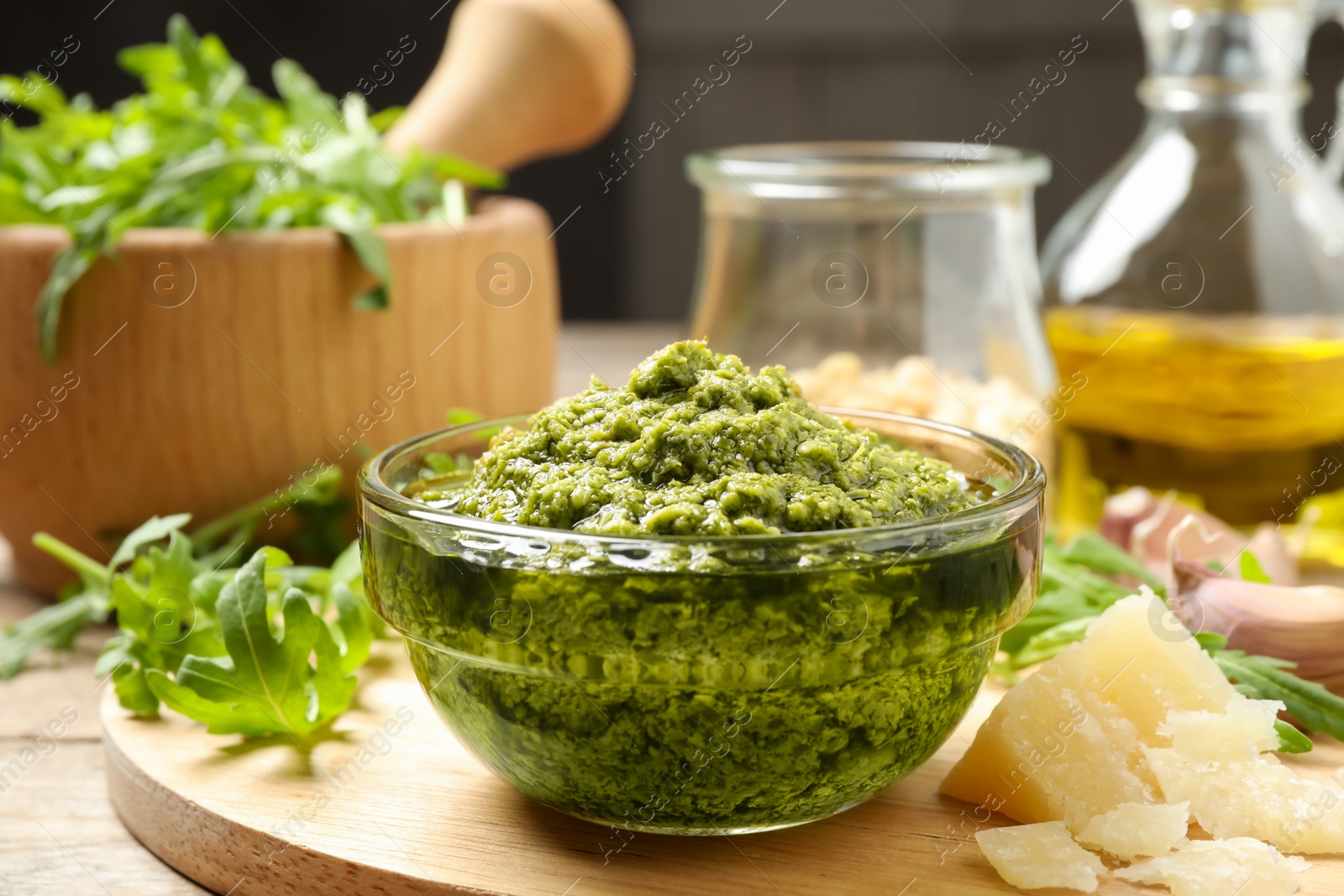 Photo of Bowl of tasty arugula pesto and ingredients on table, closeup