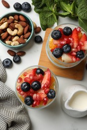 Delicious fruit salad, fresh berries, mint and nuts on white marble table, flat lay