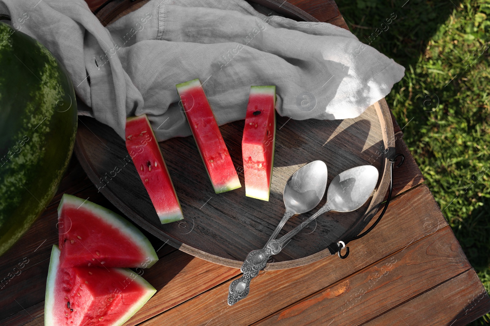 Photo of Tasty ripe watermelons and spoons on wooden table outdoors, flat lay