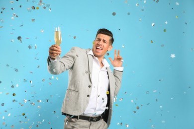 Photo of Happy man with glass of champagne and confetti on light blue background