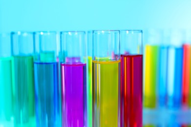 Photo of Many test tubes with colorful liquids on blurred background, closeup