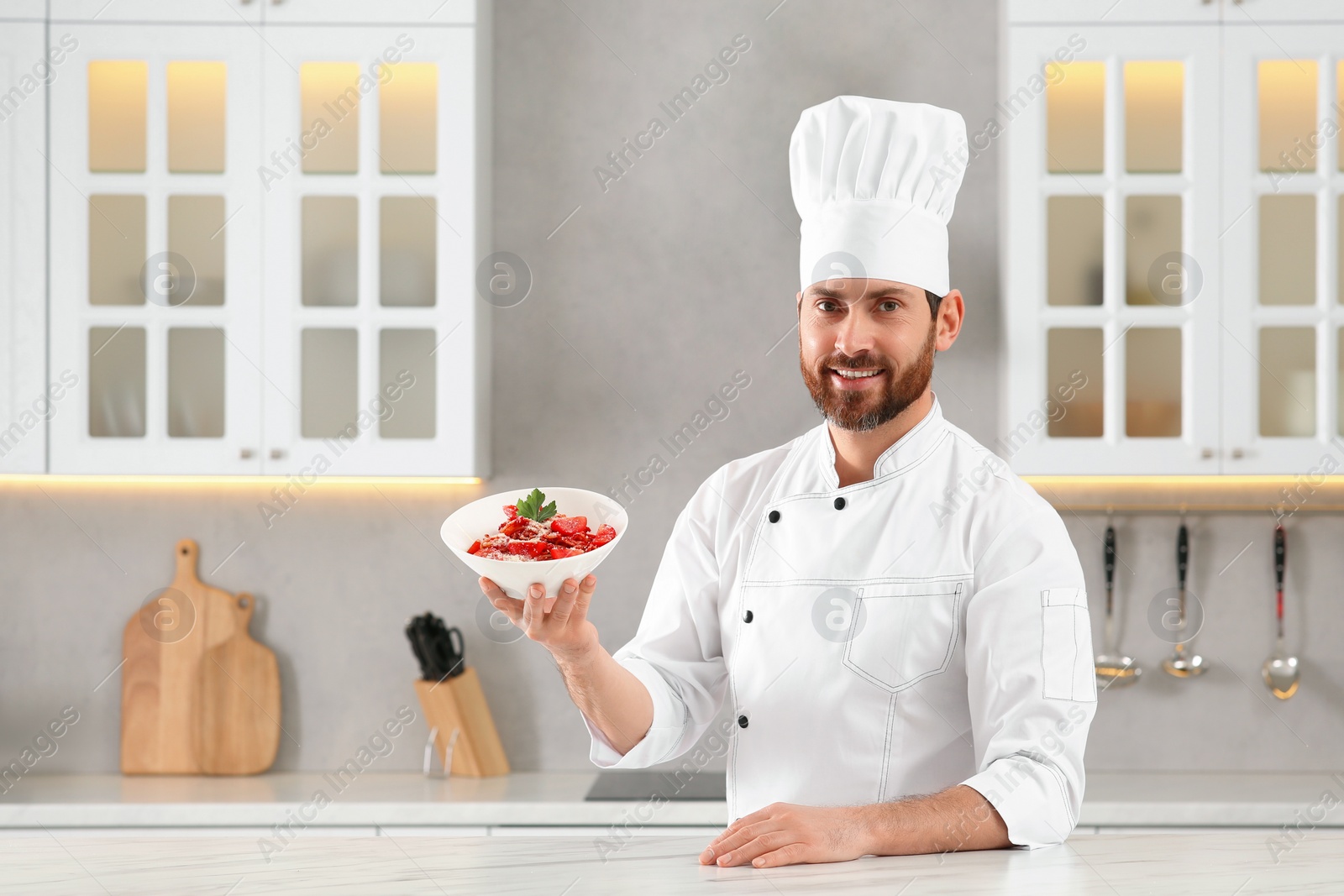 Photo of Happy chef presenting delicious dish at marble table in kitchen