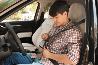 Male driver fastening safety belt in car