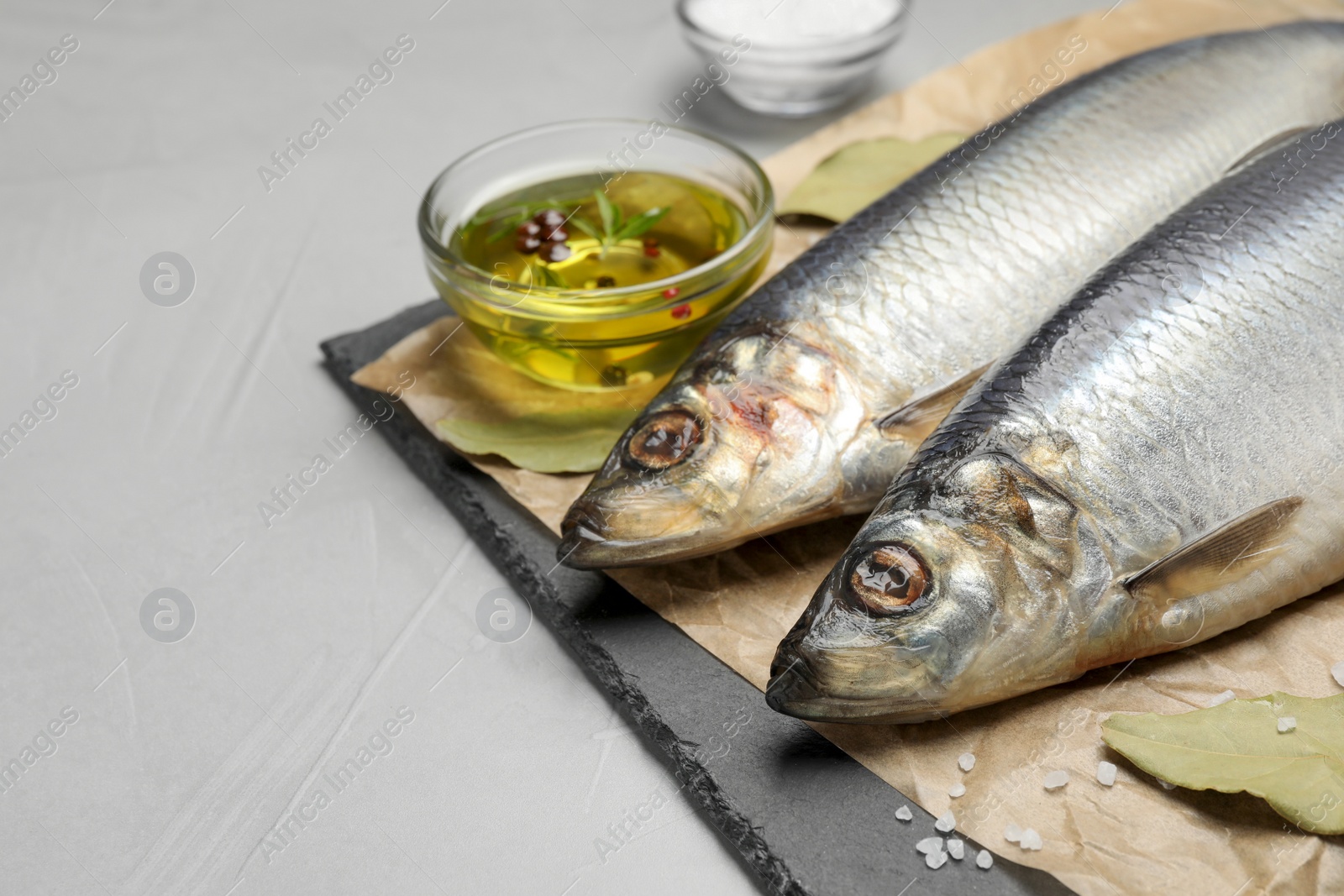 Photo of Slate plate with salted herrings, oil and spices on grey table, closeup. Space for text