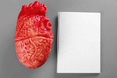 Photo of Model of heart and blank copybook on gray background. Heart attack concept