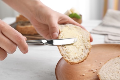 Photo of Woman spreading butter on slice of bread over table, closeup