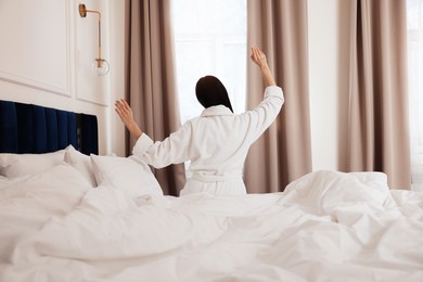 Photo of Young woman wearing bathrobe waking up in hotel room, back view