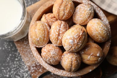 Photo of Delicious nut shaped cookies with powdered sugar and milk on black table, flat lay