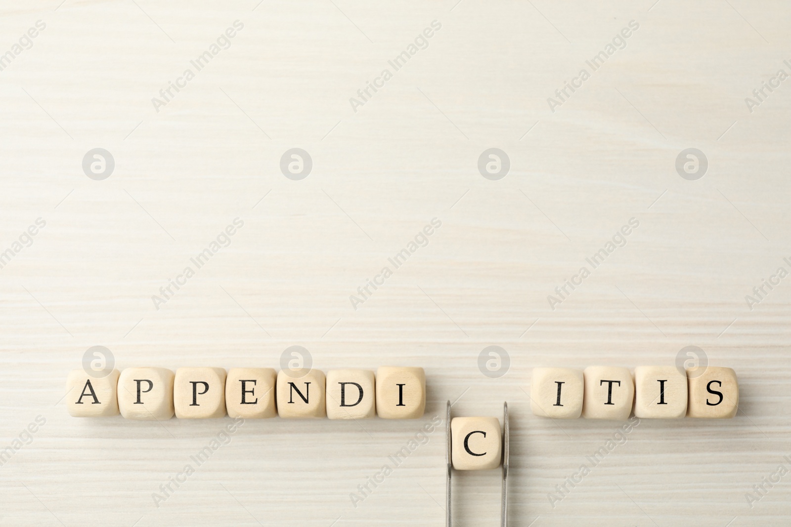 Photo of Word Appendicitis made of cubes on white wooden background, flat lay. Letter C removing with forceps