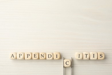 Photo of Word Appendicitis made of cubes on white wooden background, flat lay. Letter C removing with forceps