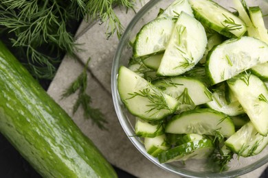 Photo of Cut cucumber with dill in glass bowl and fresh vegetables on table, flat lay