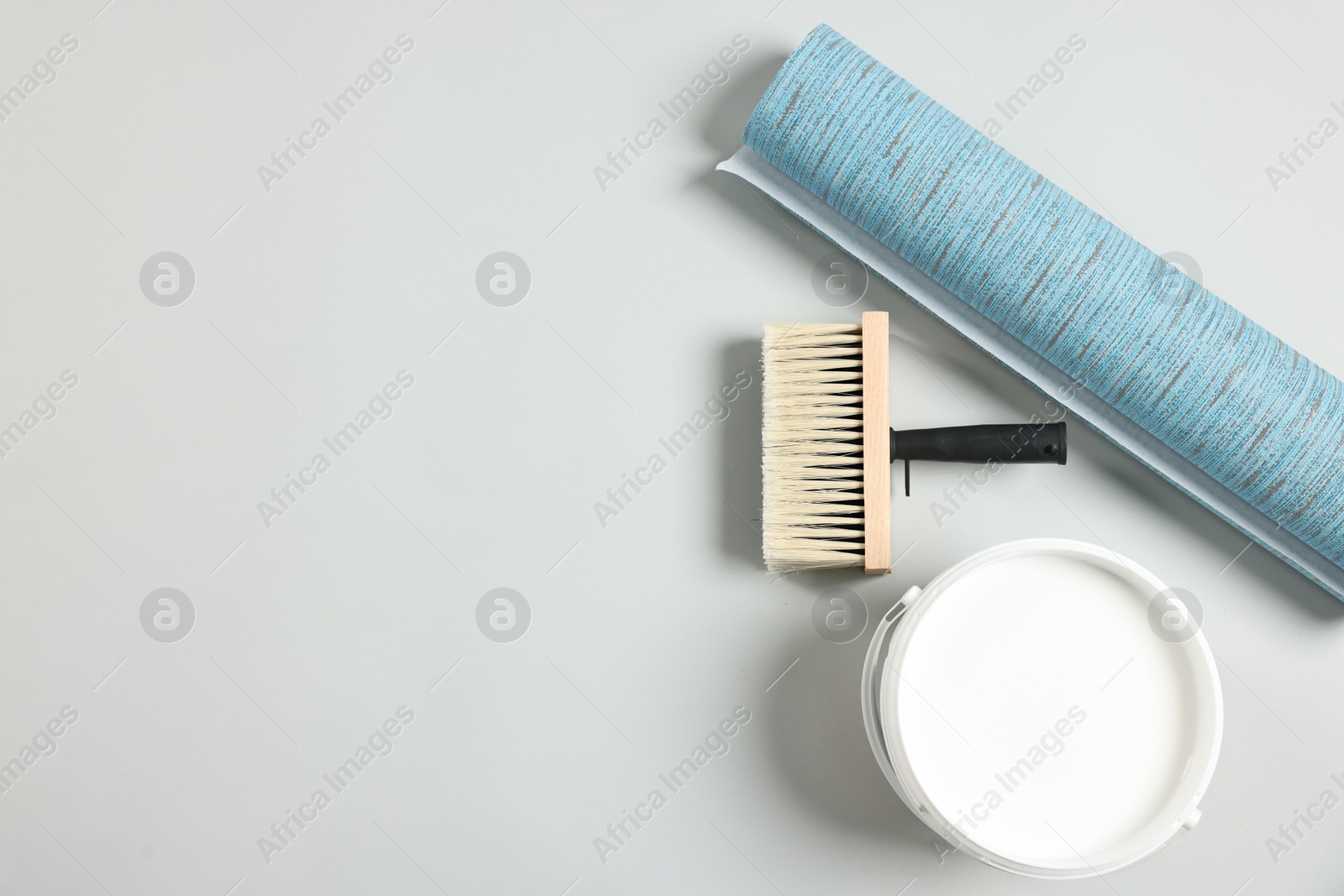 Photo of Blue wallpaper roll, brush and bucket with glue on light background, flat lay. Space for text