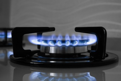 Gas burner of modern stove with burning blue flame, closeup