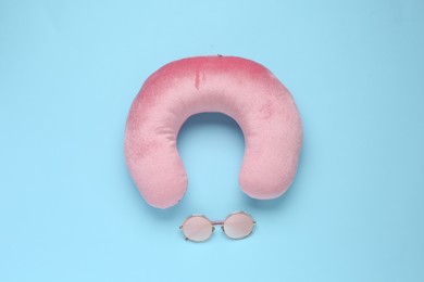 Photo of Pink travel pillow and sunglasses on light blue background, flat lay