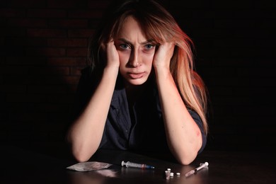 Photo of Addicted woman at table with different drugs on black background