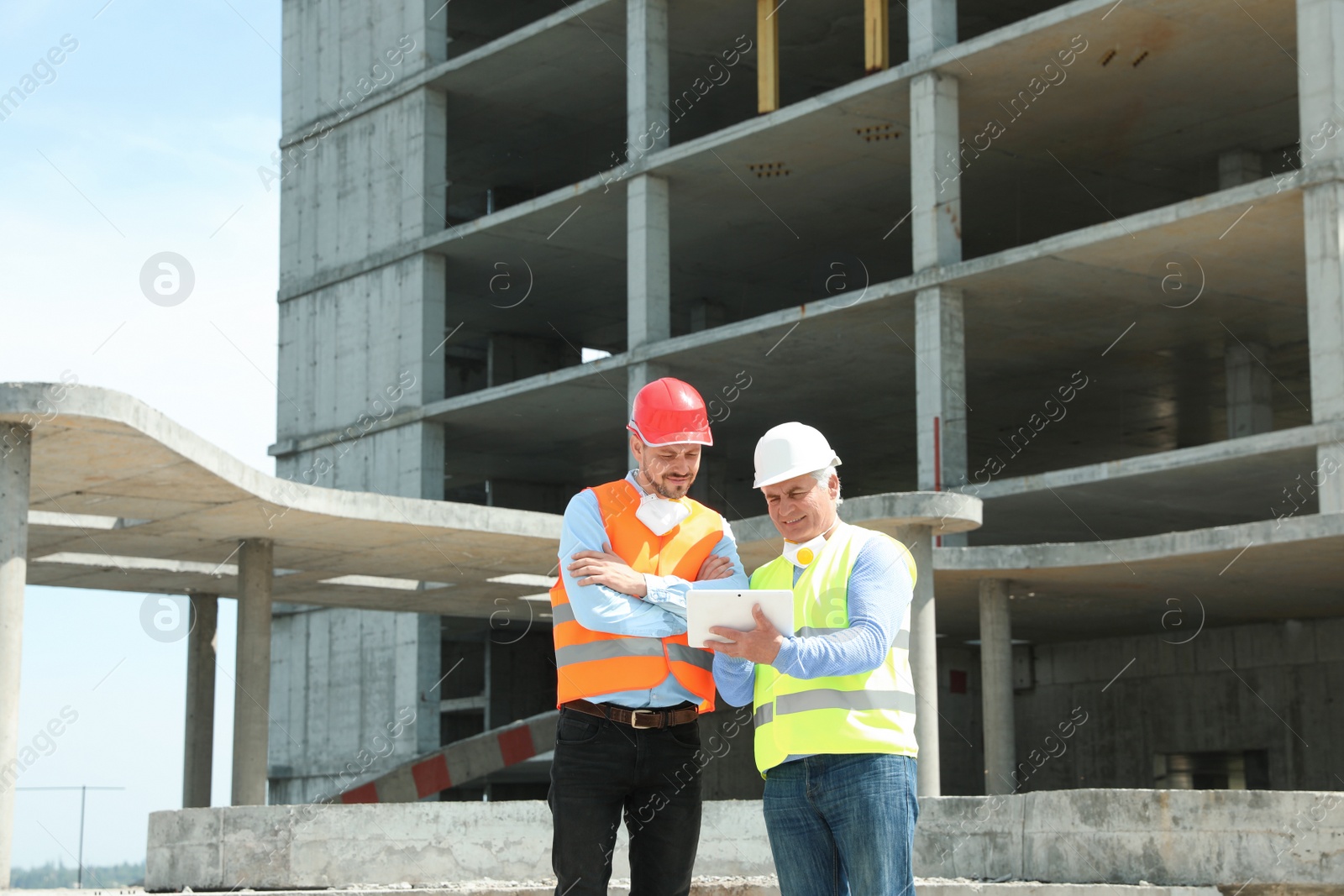 Photo of Professional engineer with tablet and foreman in safety equipment at construction site